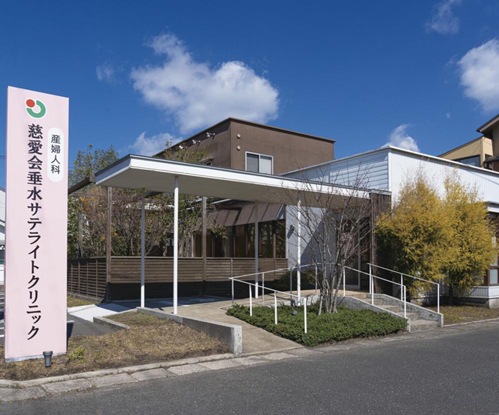 慈愛会浜水サテライトリックの建物外観。モダンな平屋建て、白と茶色の外壁、アプローチに施設名看板。